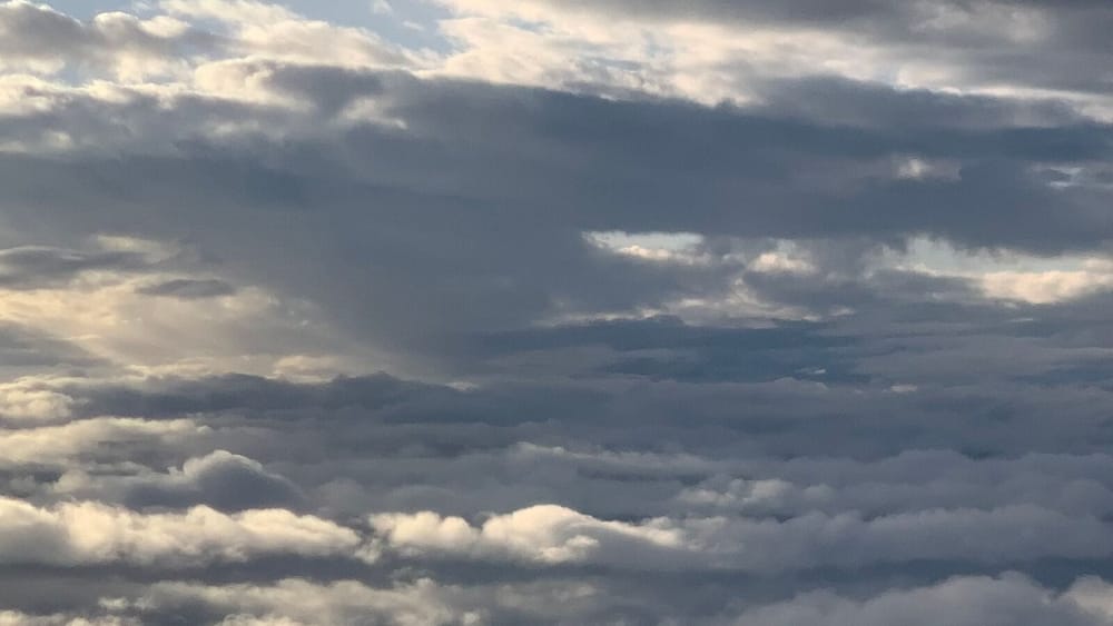 Layered clouds seen from a plane window, with sunlight breaking through on the left